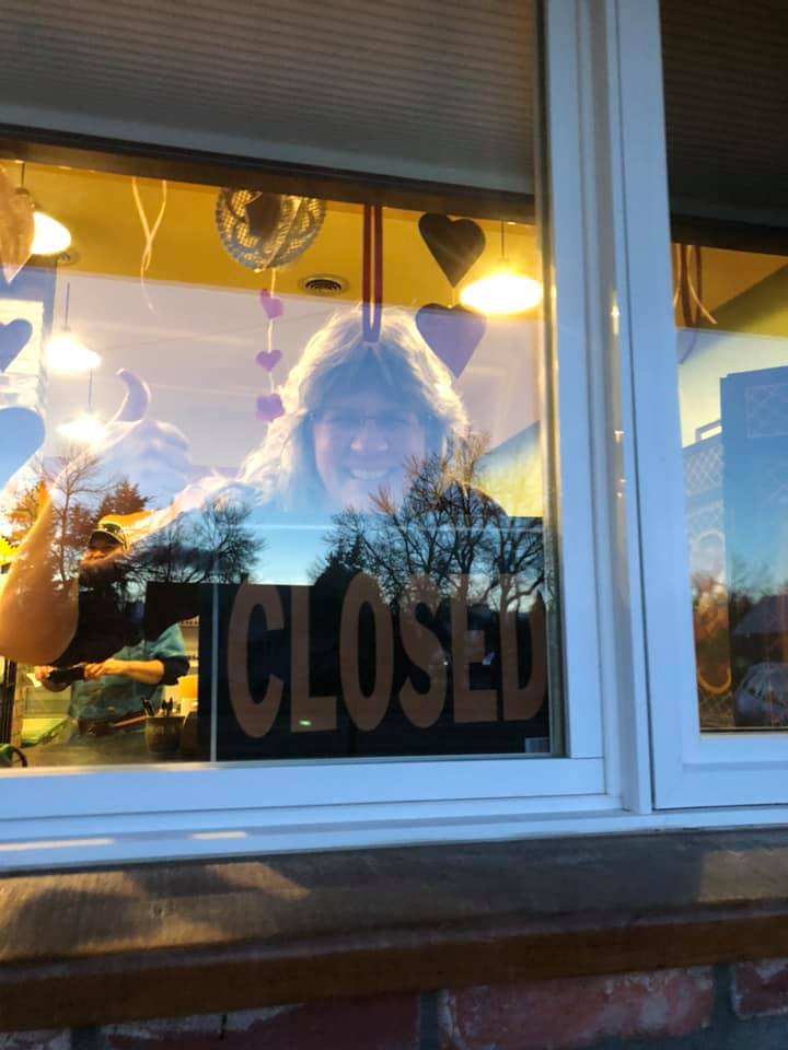 Jill Owen waving goodbye behind the closed sign of the Mountain Front Market